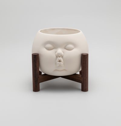 ceramic pot in form of babies face, on wooden stand