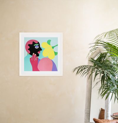 a print edition in a white frame hung next to a plant