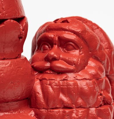 a close-up detail of a bronze santa holding a christmas tree shaped butt plug painted in red