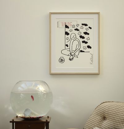 framed print on a pale wall above a comfy-looking chair and a large round fishbowl