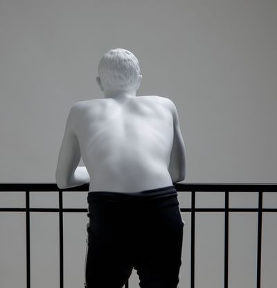 topless figure seen from behind, leaning on railing of black metal balcony