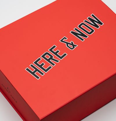 bright red box emblazoned with 'HERE & NOW' in black and white
