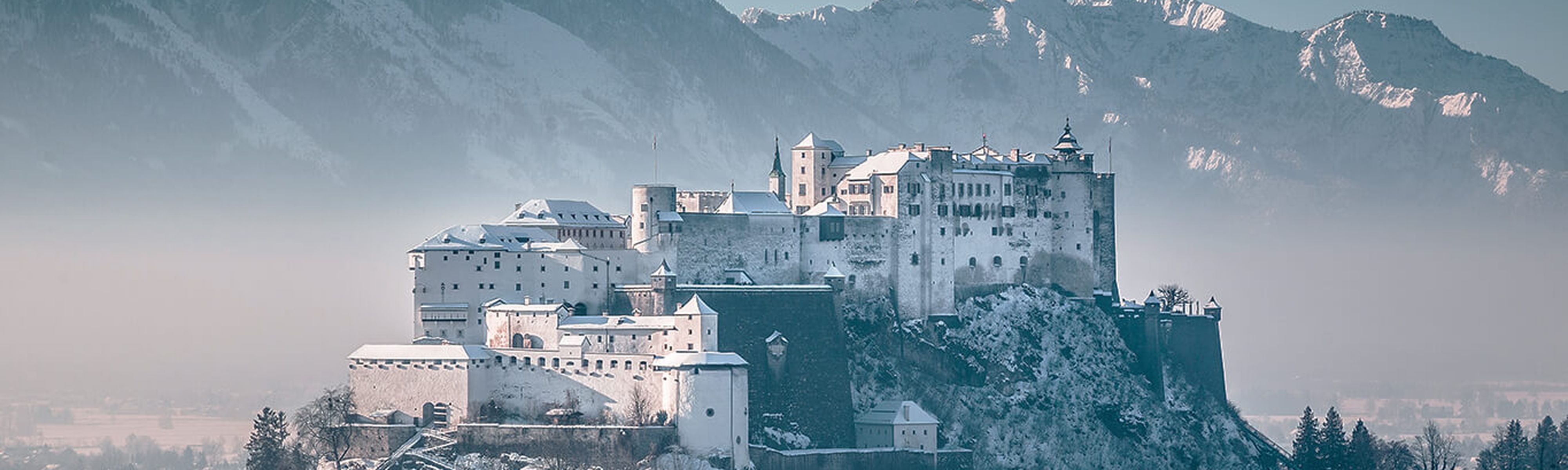 hohensalzburg castle in austria surrounded by snow capped mountains