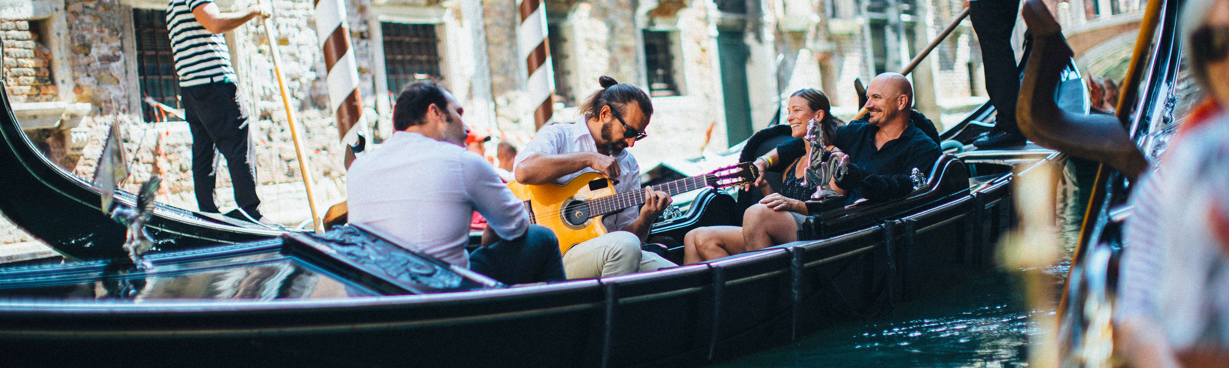 couple riding in a gondala listening to a man playing guitar in venice italy