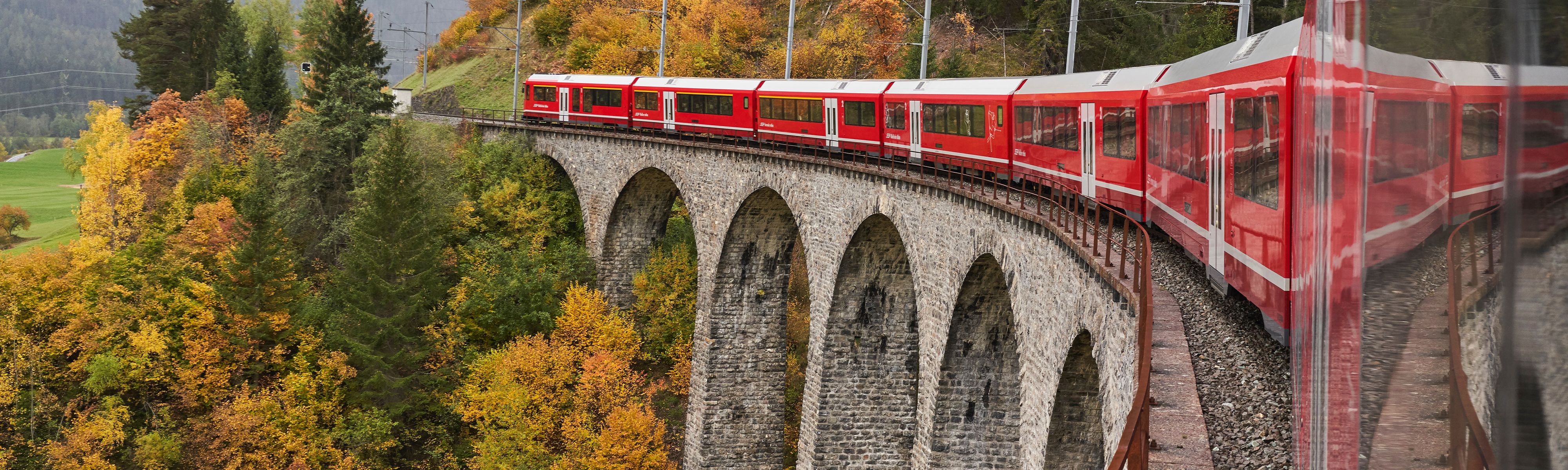 bright red train riding over a bridge in Switzerland