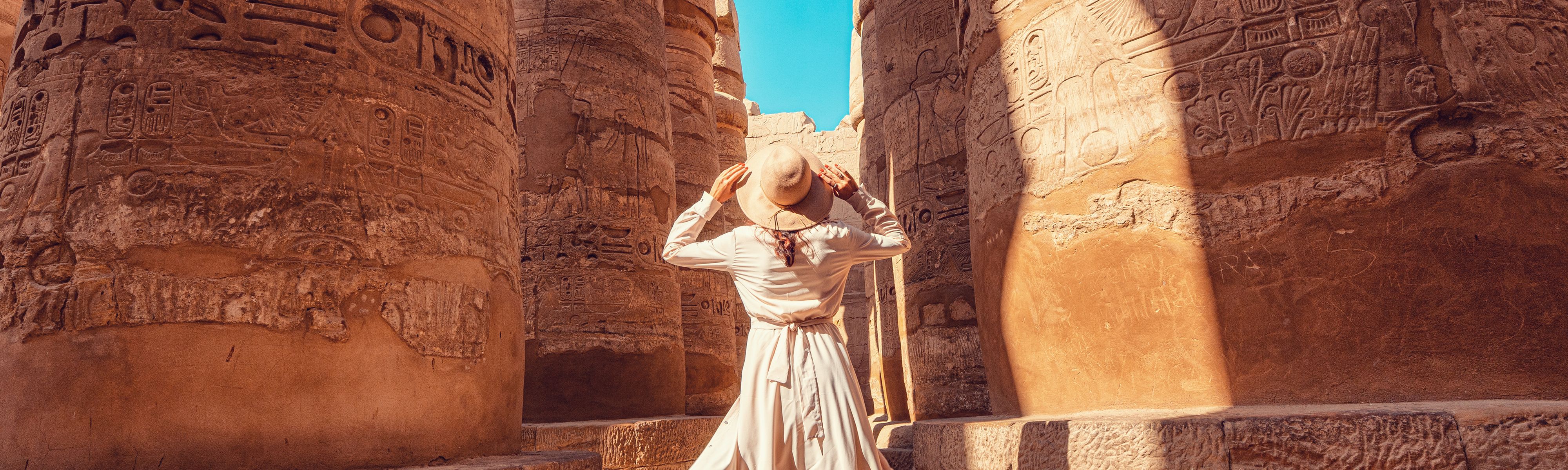 woman holding her tan hat looking up at the pillars in egypt