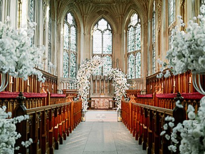A gothic chapel is decorated with white flowers and a floral arch in the middle