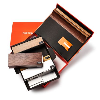 An open orange Fortina sample box. Inside the box are various materials Fortina panels are made up of as well as an orange business card.