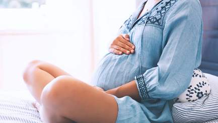 Schwangere Frau mit erhöhtem Magnesiumbedarf sitzt im Schneidersitz auf dem Bett