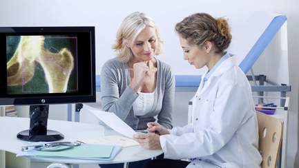 Ärztin sitzt mit Patientin an einem Tisch und bespricht eine Osteoporose-Diagnose