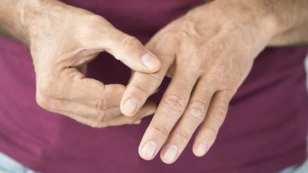 Mann mit rheumatoider Arthritis fasst sich an schmerzenden Zeigefinger