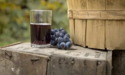 Glass of Welch's grape juice on an apple box, next to a bunch of grapes