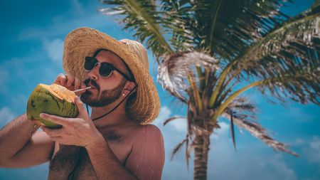A man drinking out of a coconut on a beach.