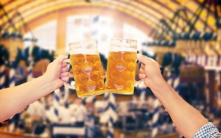 Two beer steins being cheers'd in an Oktoberfest tent.