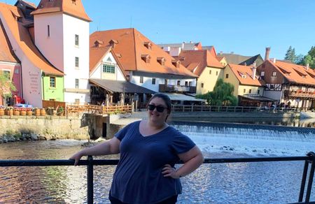 A plus-size woman smiling as she poses along a canal in a European village.