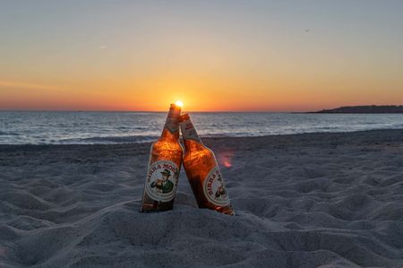 Two bottles of a local Italian beer, Birra Moretti, sitting in the sand on a beach.