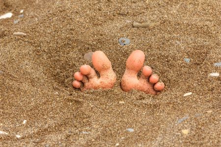 A person's feet sticking out of the sand.