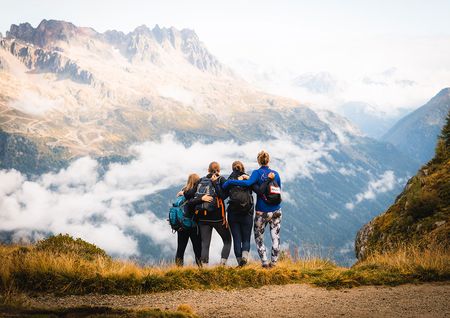 Four girls standing at the top of a mountain gazing at clouds and peaks in the distance.