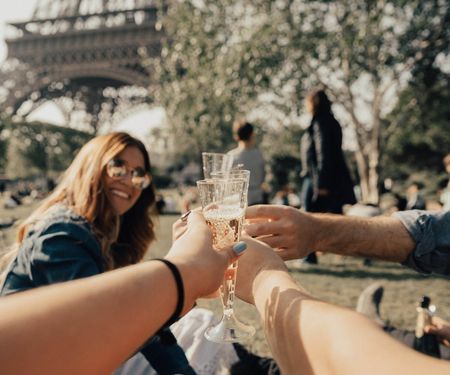 Three friends clanking their champagne glasses together under the Eiffel Tower in Paris.