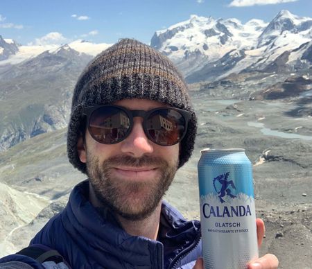 A hiker in the Alps holding up a can of glacier water.