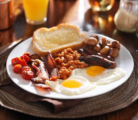 A full English breakfast with eggs, sausage, bacon, potatoes, bread, and beans.