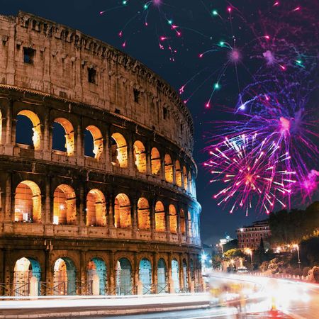 The Roman Colosseum at night with fireworks exploding in the sky above it.