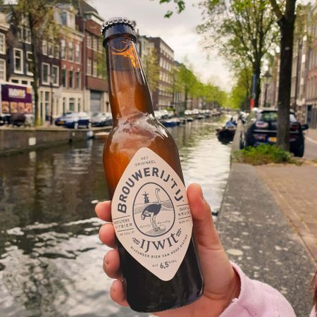 Someone holding a local Amsterdam beer bottle while standing by the city's famous canals.