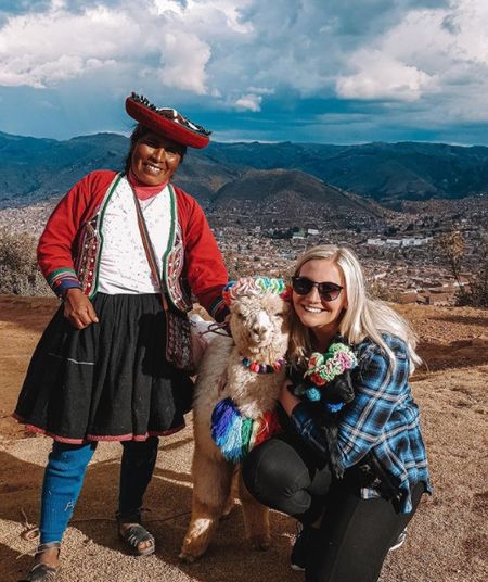 A young woman petting an alpaca and talking to a local Peruvian woman.