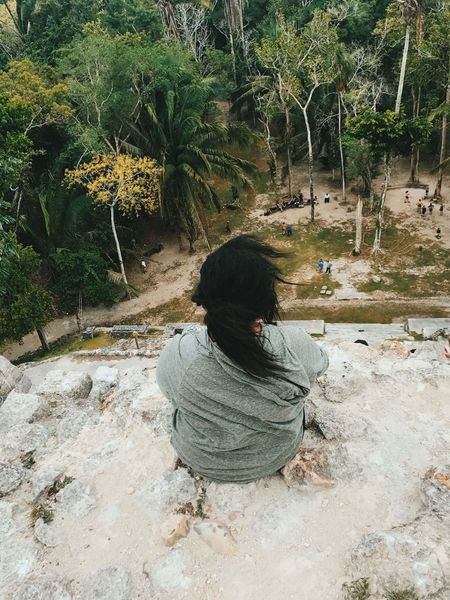 A girl sitting on top of an ancient Mayan citadel, looking down.