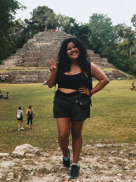 A girl standing in front of ancient Mayan ruins.