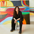 Marina Perez Simao sitting on a chair in front of several colourful paintings