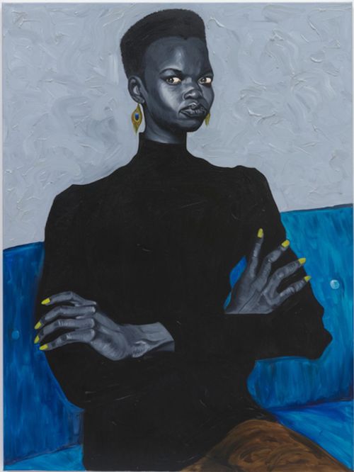woman with bright yellow finger nails sits on a blue sofa with her arms crossed in front of her