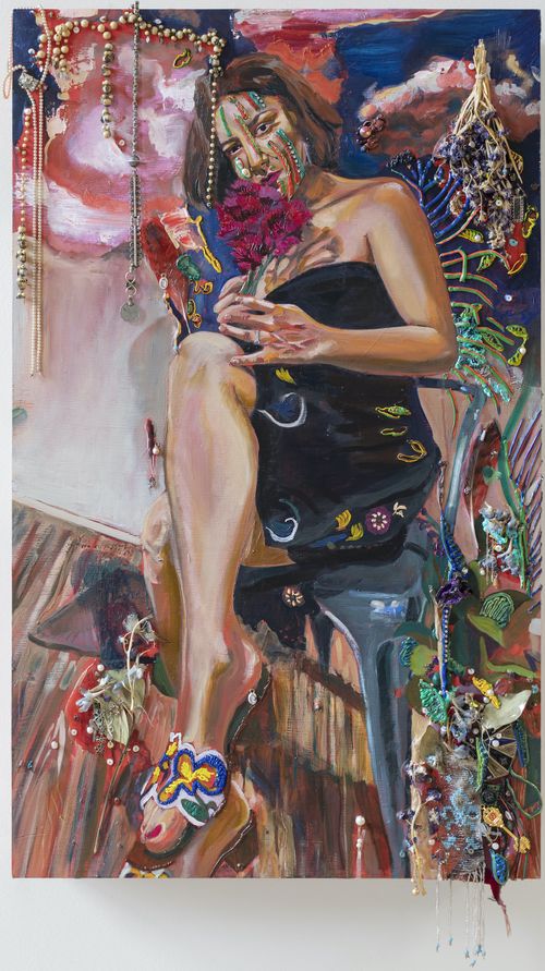 woman wearing black strapless dress with sandals seated on a chair with a pink flower in her hand, surrounded by beads and plants