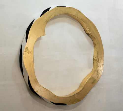 a striped hollow circle with a gold frontal frame set against a wall