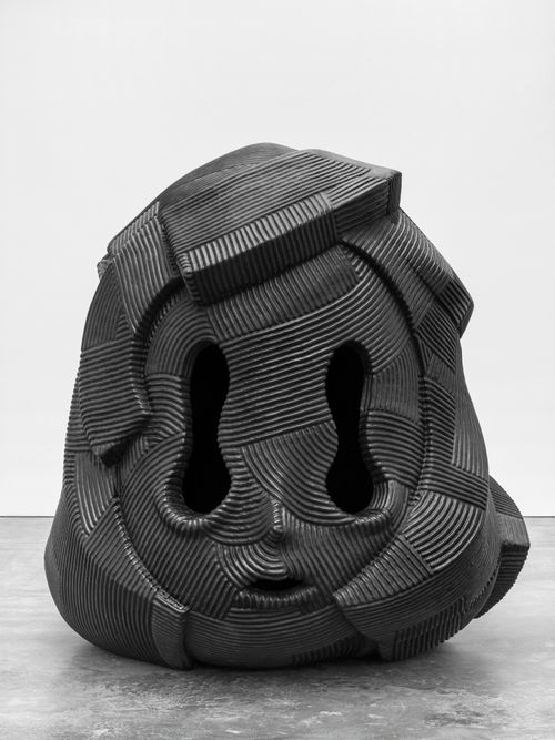 Black textured sculpture with drooped eyes sitting on a grey floor