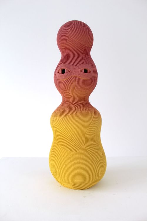 Tall curved sculpture with eyes, peach colours fading into yellow