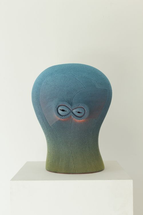 Blue fading to green, curved sculpture with eyes on white plinth