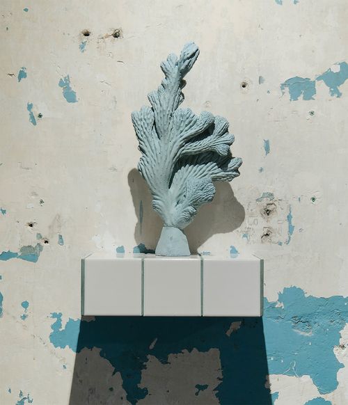 blue sculpture of a cactus on a white ledge against a white wall with areas of blue
