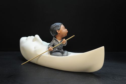 a sculpted face with the forehead extended into the shape of a long boat, on which a man sits and rows with a long stick in his hand