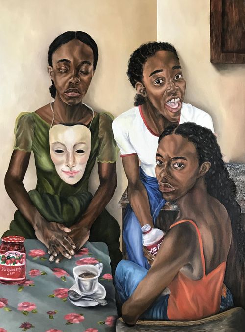 three girls, one with a theatrical mask around her neck, sit around a table which has a cup of tea and a jar of strawberry jam on it