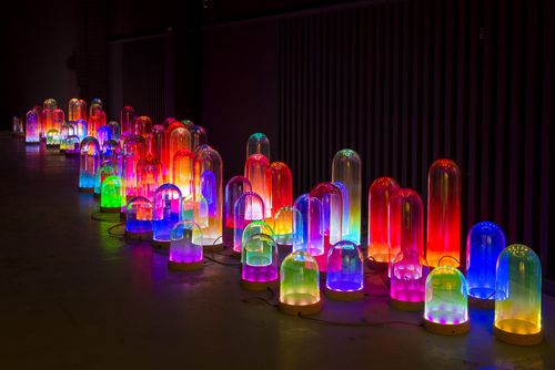 a dark space illuminated by cylindrical lanterns of varying sizes and colours
