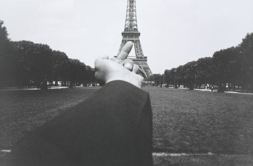 a monochrome photograph of artist Ai Weiwei sticking his middle finger up at the Eiffel Tower in Paris