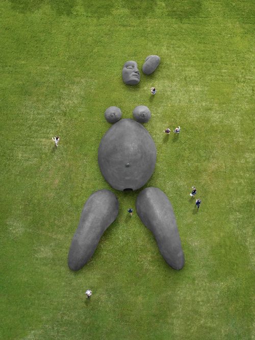 a giant brick sculpture of a pregnant woman emerging from green grass-covered earth