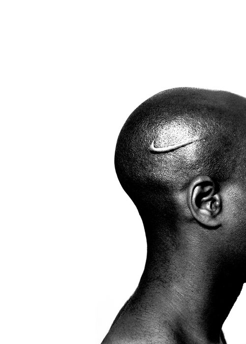 head of a black man shown from a side profile, with no hair and a nike logo tick rising from the skin of their head