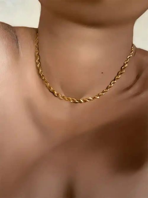 bare female décolletage focusing on a gold twisted chain necklace that hangs around the woman's neckline