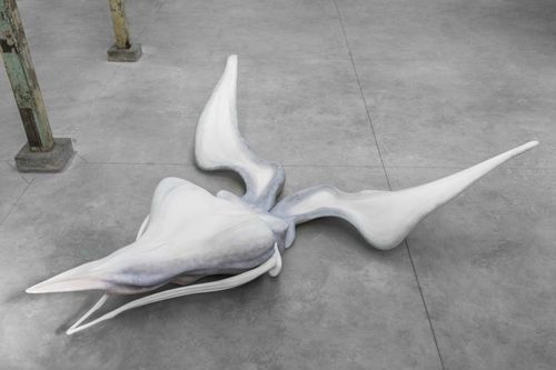 white sculpture resting on the floor of a gallery