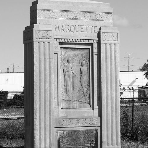 Framed by a stylized, art deco influenced pylon that was once integrated into the former bridge’s architecture, a low relief bronze shows the ethereal figure of Pere Marquette, his hand outstretched to greet an American Indian warrior in a wooded, riverside setting. Marquette is wearing clerical robes, while the Indian, who salutes Marquette, is minimally covered to reveal his strong musculature.