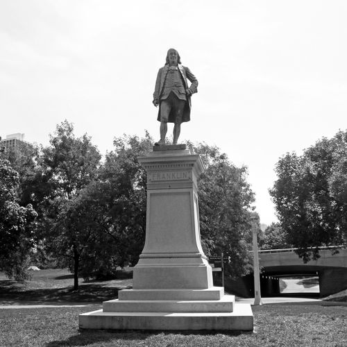Standing with his left hand on his engaged hip, the other falling casually to his right side, Franklin appears at the summit of a slender, stepped pedestal, high above our heads.