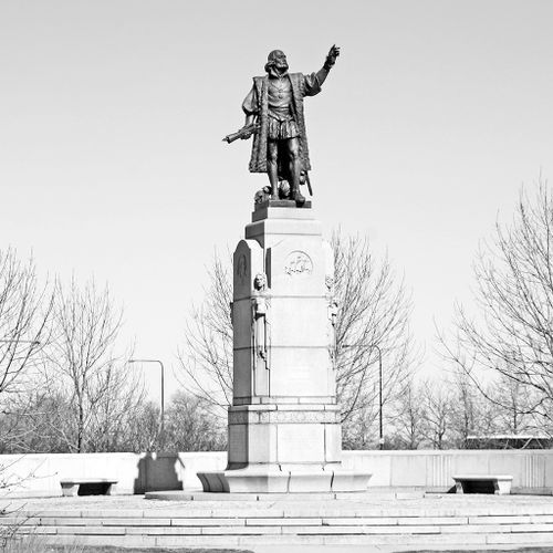 The largest of the Columbus monuments, this work sits atop a very high, elaborately carved stone pedestal set atop a broad plinth. The figure of Columbus is attired in elaborate robes, more suitable for a royal court. He raises his left arm high with open hand and holds a scroll in his right hand. Bearded and with a receding hairline, he looks older, but still vital and rugged.