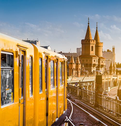 An orange train on traintracks with a grand ornate building in the background with multiple pointed domes
